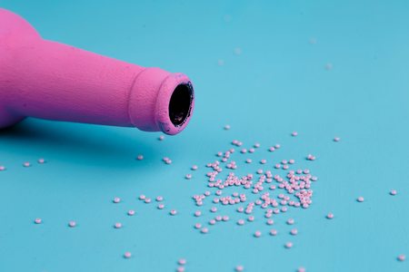 Pink bottle and sprinkled beads on blue background. Alcoholism,の写真素材