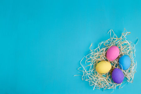 Multicolored Easter eggs in hay, flat lay with copy space