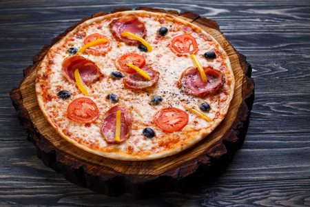 Appetizing sicilian pizza with bacon, olives and tomatoes servedの写真素材