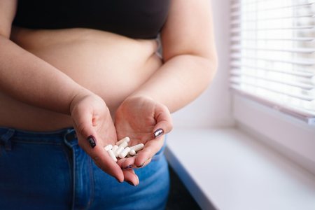 Overweight woman doubting to take slimming pills. Unhealthy wayの写真素材