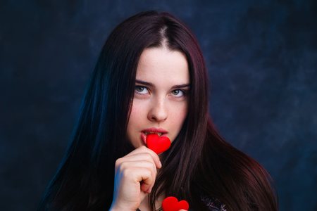 Young cute girl holding in hands and biting fabric hearts, studiの写真素材