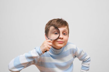 Cute boy looking at camera through magnifying glass, on white baの写真素材