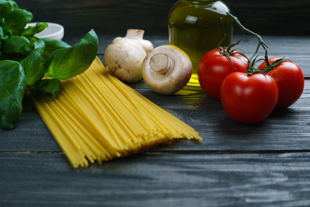 Pasta cooking ingredients. Raw spaghetti, tomatoes, basil, olive oil, mushrooms and spices on wooden table, close up. Italian cuisine food background conceptの写真素材