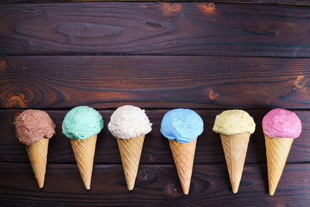Various ice cream cones on wooden table, flat lay