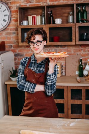 Young woman with fresh pizza at her kitchenの写真素材