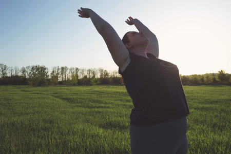 Young overweight woman doing yoga at summer meadow