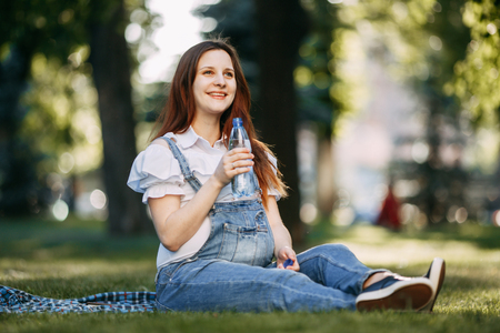 Pregnant woman resting at park drinking waterの写真素材