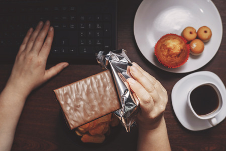 Woman eat chocolate and sugary food at workplaceの写真素材