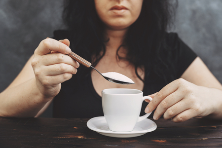 woman pouring sugar into coffee cupの写真素材