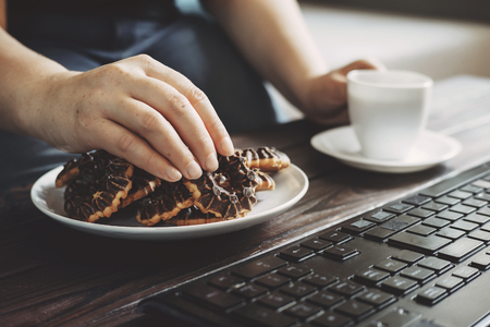 Woman eating cookies and coffee at workplaceの写真素材