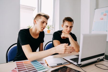 Two young men looking at laptop monitor discussing