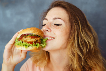 young woman eating greedily delicious burgerの写真素材
