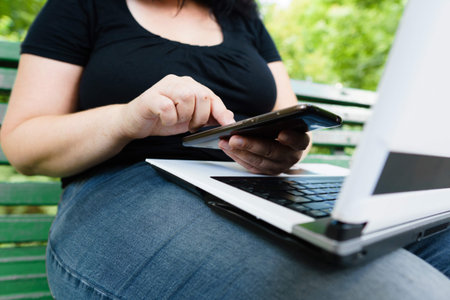 woman with smart phone and laptop working outdoors