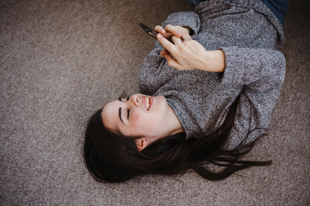 Cheerful woman typing on mobile phone at homeの写真素材