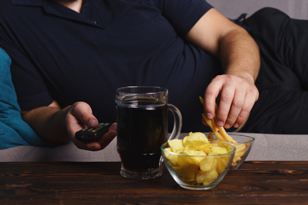 Overweight man with tv remote, junk food and beerの写真素材