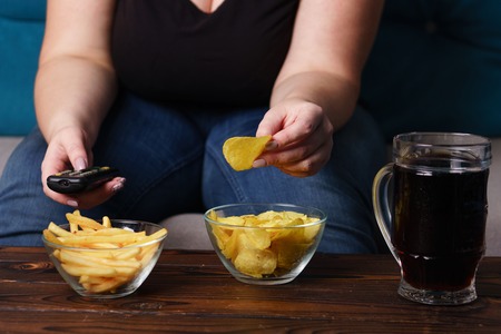 Obese woman with tv remote, junk food and beerの写真素材