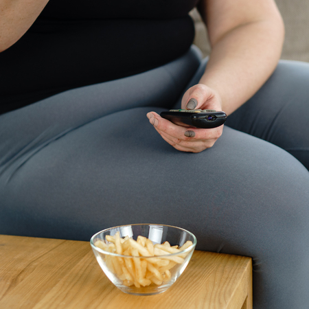 Fat woman watching series at tv eating junk foodの写真素材