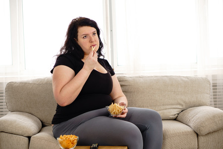 Fat woman watching series at tv eating junk foodの写真素材