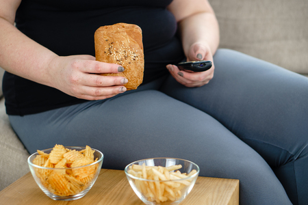 Fat woman watching series at tv eating junk foodの写真素材