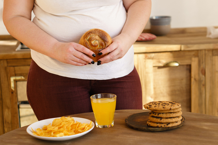 Overweight woman eating sugary foods drinking sodaの写真素材