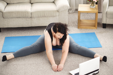 Overweight woman doing stretching exercise at homeの写真素材