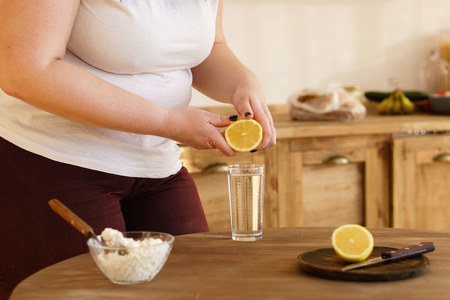 Overweight woman squeezing lemon juice into waterの写真素材