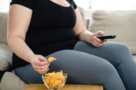 Overweight woman with tv remote and junk foodの写真素材