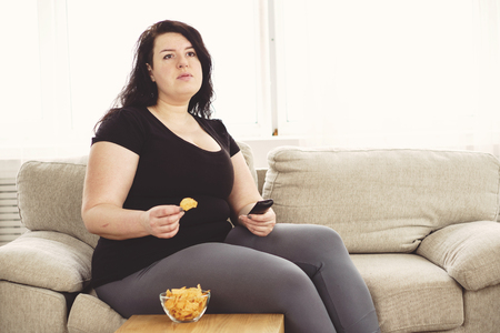 Overweight woman with tv remote and junk foodの写真素材