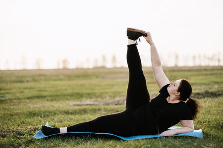 Overweight woman training legs on yoga mat outdoor
