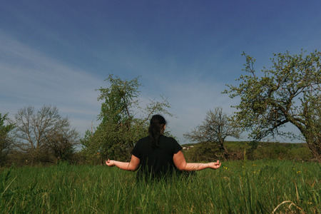 Overweight woman meditating sitting in the meadowの写真素材