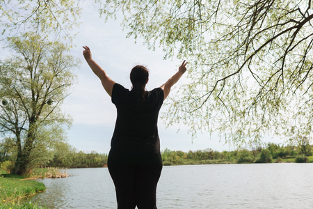 Overweight woman rising hands, view from the backの写真素材