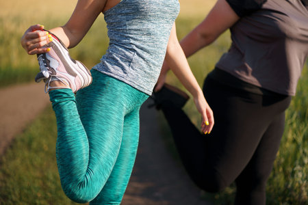 Overweight and fit women warming up before outdoor jogging. Two female friends getting ready for...