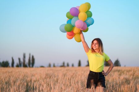 Happy young woman with colorful balloons in summer fieldの写真素材