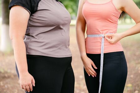 Fat and slim woman measuring waistline with tapeの写真素材