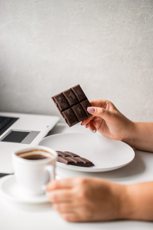 Woman eating chocolate and coffee at workplace