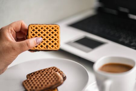 Woman eating cookies and coffee at workplaceの写真素材