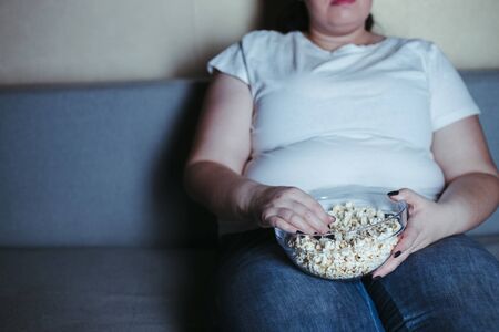 Overweight woman sit on the coach with junk foodの写真素材