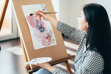 Young woman sitting at easel painting with watercolorsの写真素材