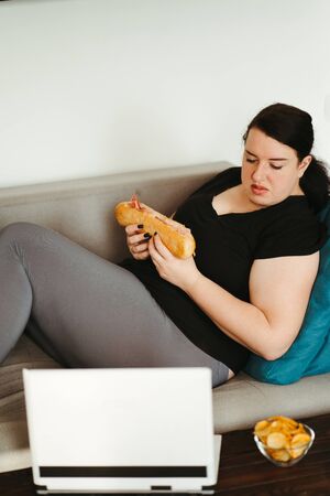 Woman eating unhealthy food watching series onlineの写真素材