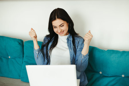 Young excited lady using laptop in living roomの写真素材