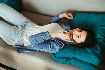 Cheerful woman talking on mobile phone at homeの写真素材