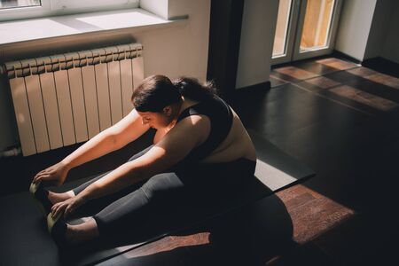 Overweight woman doing yoga exercise at homeの写真素材