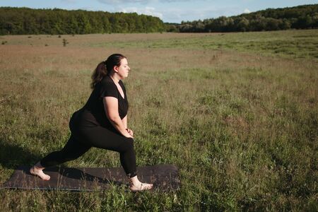 Overweight woman doing yoga exercises in natureの写真素材