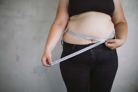 Overweight woman measuring waist with measure tapeの写真素材