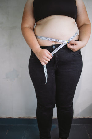 Overweight woman measuring waist with measure tape