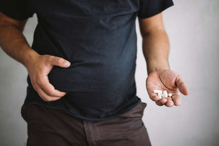 Overweight man holding slimming pillsの写真素材
