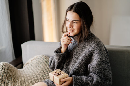 Woman with present box sitting in living roomの写真素材