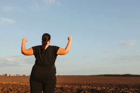 Overweight woman rising hands, view from the backの写真素材