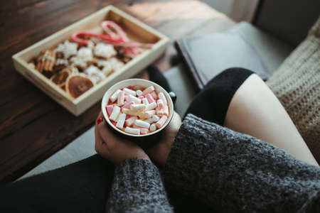 Hygge, Christmas holidays. Cozy home concept. Woman eating festive sweets with hot chocolate. Winter warming drinkの写真素材