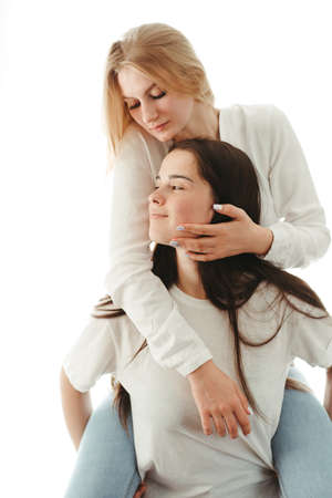 Happy playful girlfriends in love sharing time together indoors giving a piggyback hug. Human relationships, fun, friendship, supportの写真素材